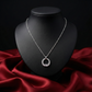 Silver necklace with a circular pendant on a black mannequin bust against a red fabric background