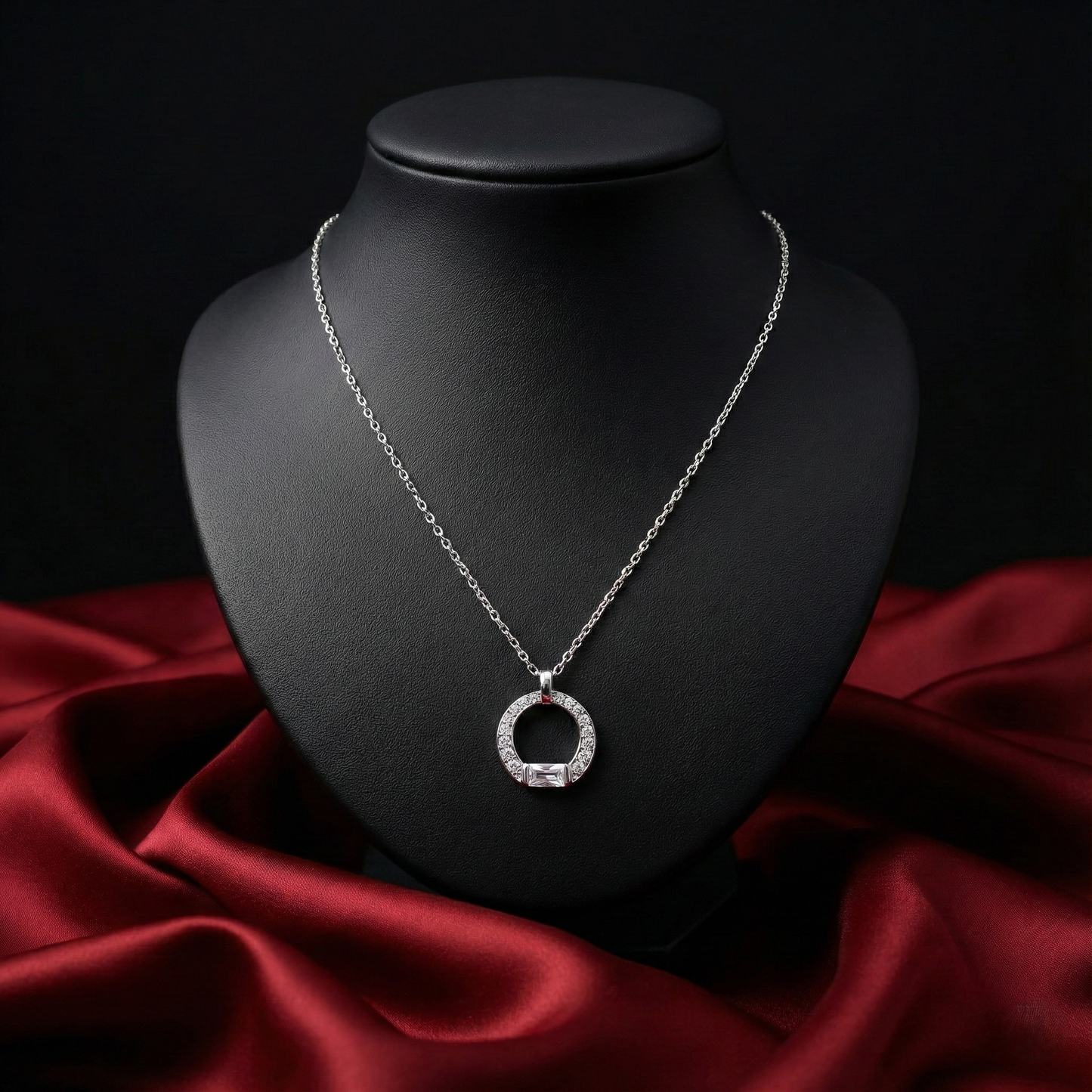 Silver necklace with a circular pendant on a black mannequin bust against a red fabric background