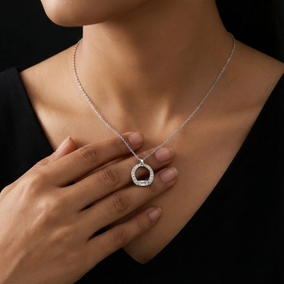 Silver necklace with a circular pendant worn by a person against a black background