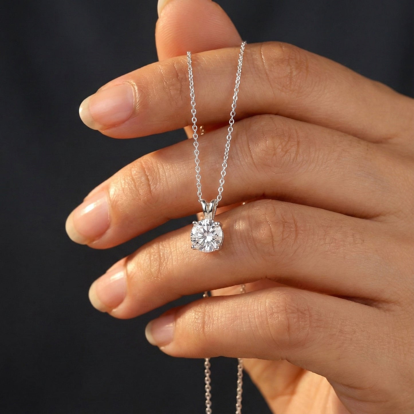 Hand holding a silver necklace with a diamond pendant against a dark background