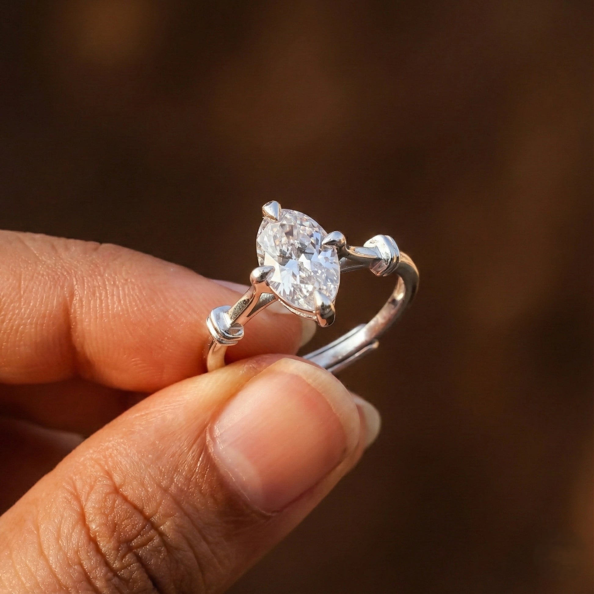 Silver ring with a large diamond held between fingers against a blurred brown background