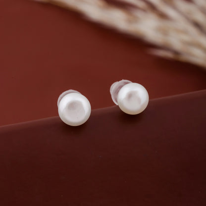 Pair of white pearl stud earrings with smooth round finish on a brown background