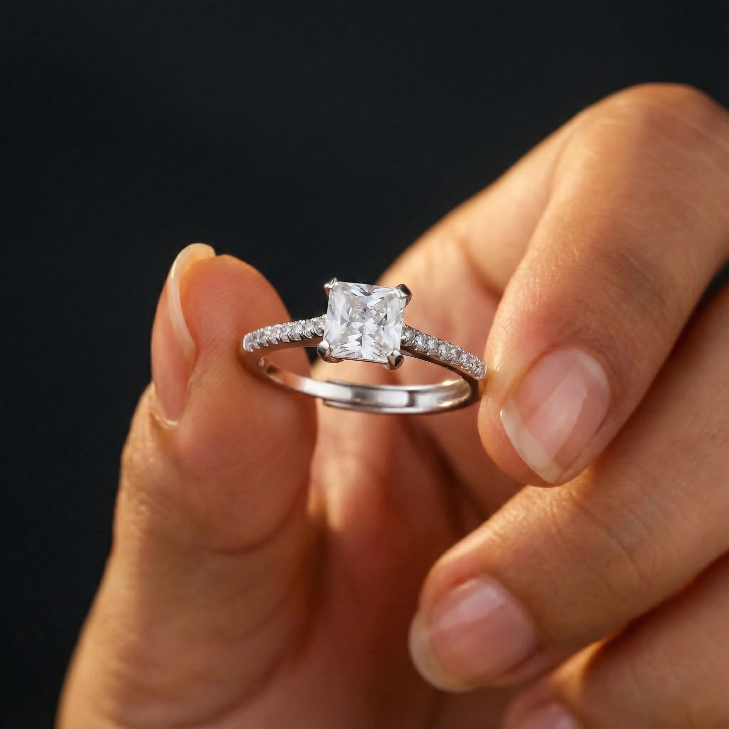 Diamond ring held between fingers against a dark background