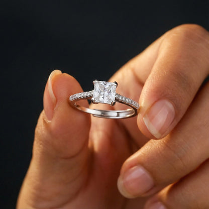 Diamond ring held between fingers against a dark background