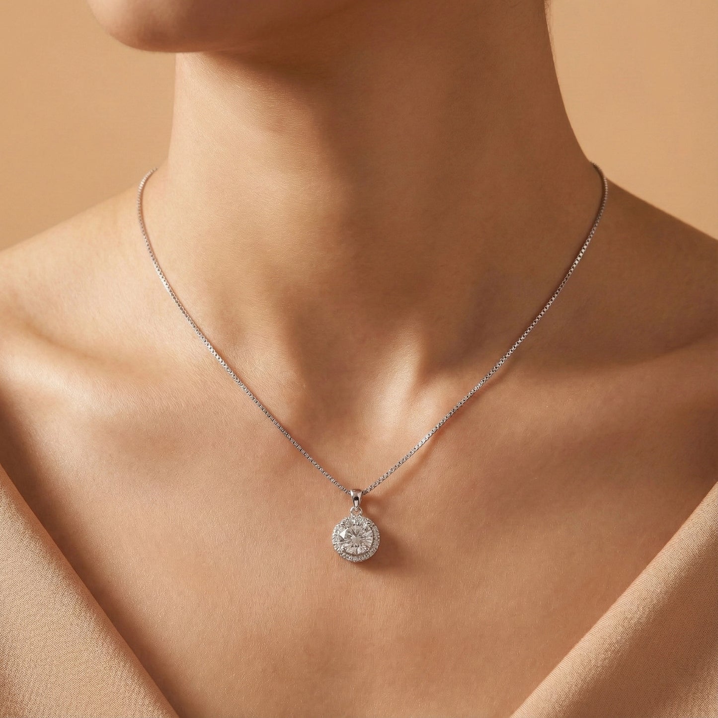 Silver necklace with a round pendant on a person against a beige background