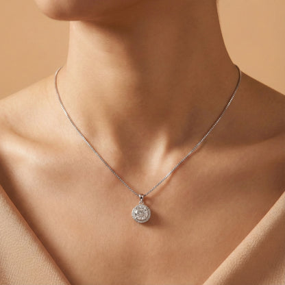 Silver necklace with a round pendant on a person against a beige background