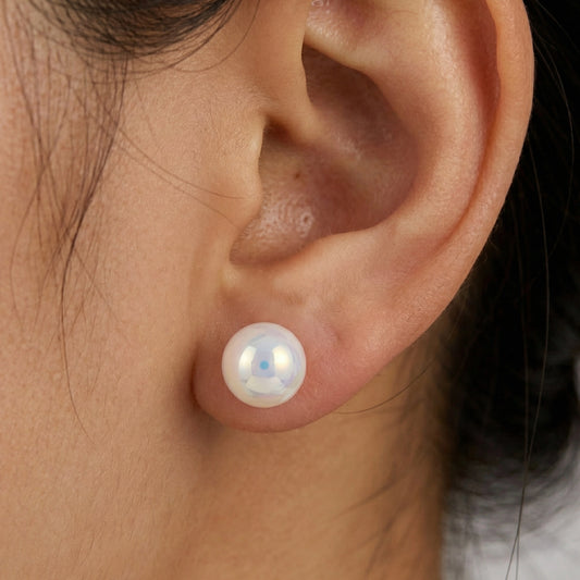 Close-up of iridescent pearl stud earrings with glossy round surface on a brown background