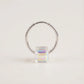 Silver hoop earring with a colorful square gemstone on a light beige background