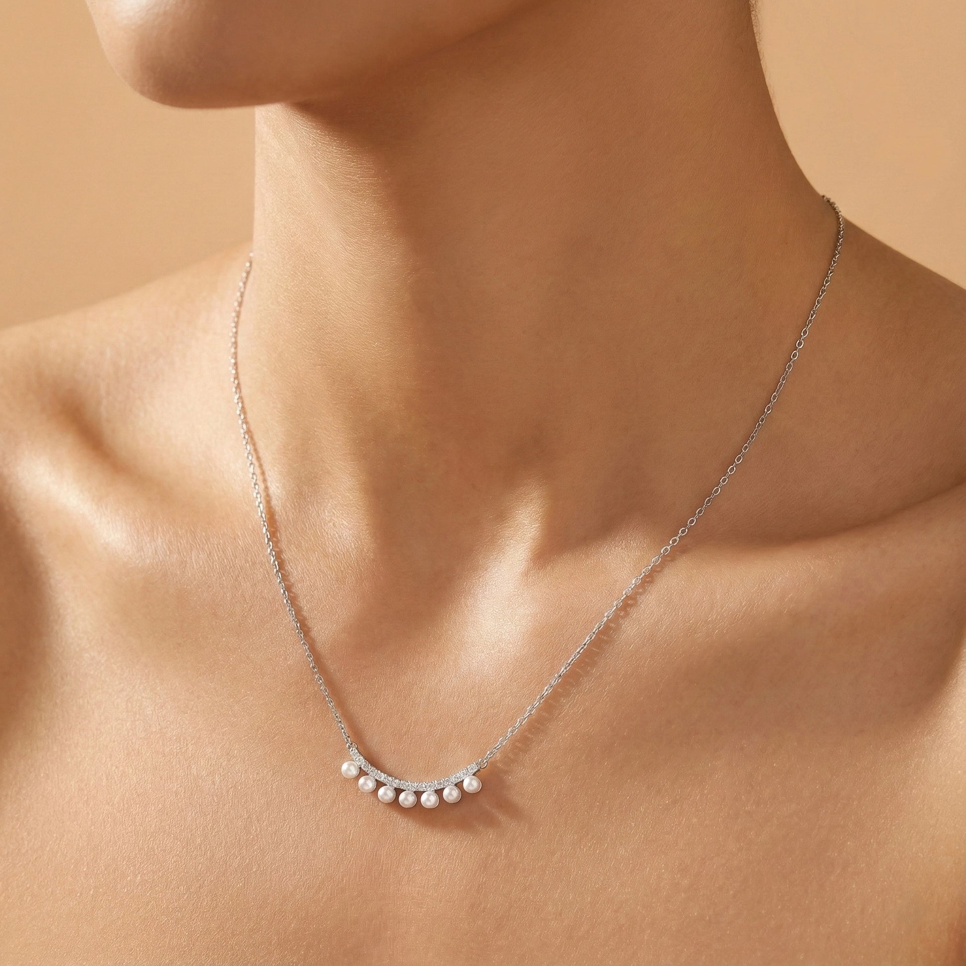 Silver necklace with small pearls on a person's neck against a beige background