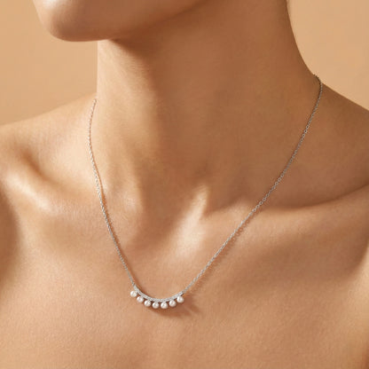 Silver necklace with small pearls on a person's neck against a beige background