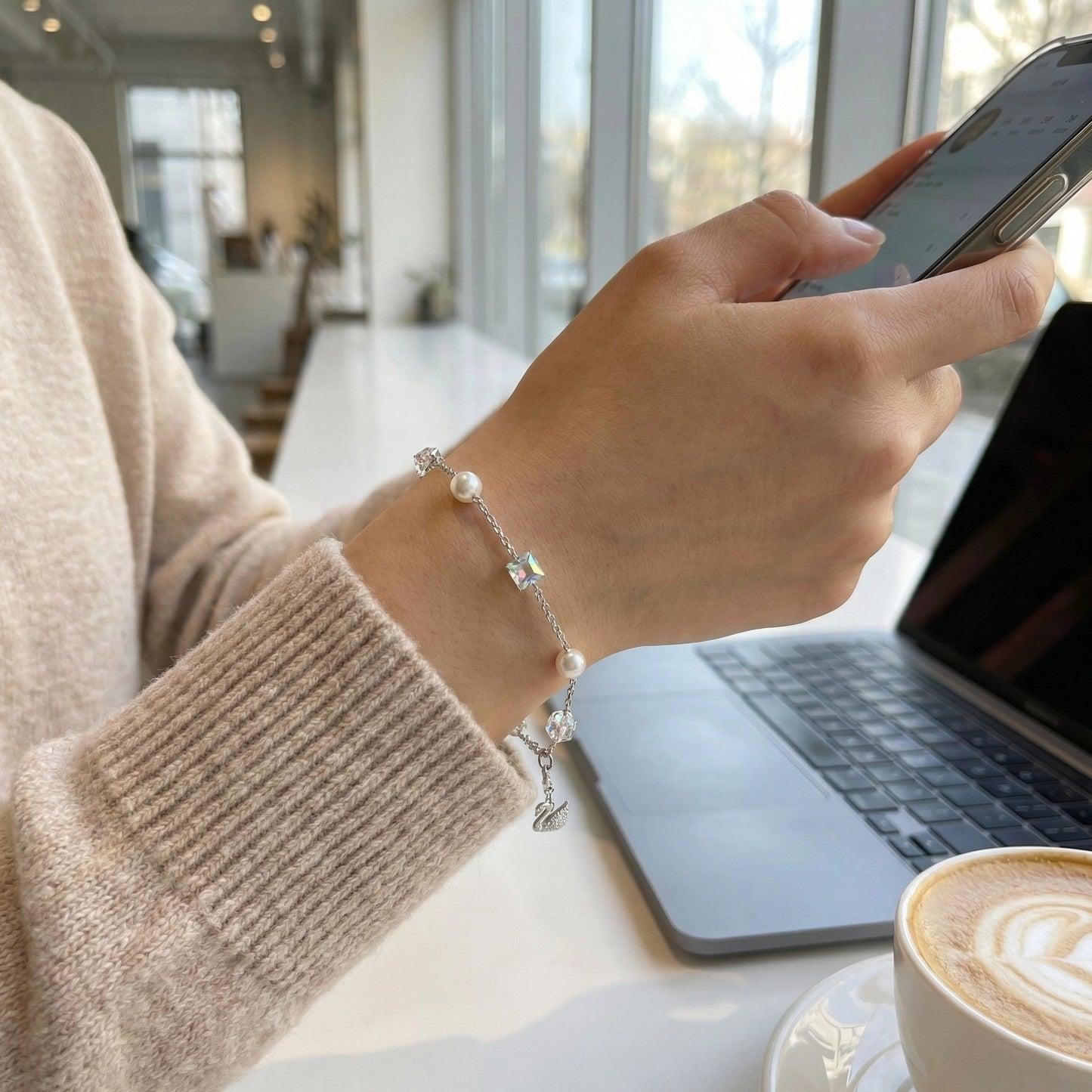 Person using a smartphone with a laptop and a cup of coffee in the background