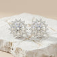 Pair of silver snowflake-shaped earrings on a textured white surface