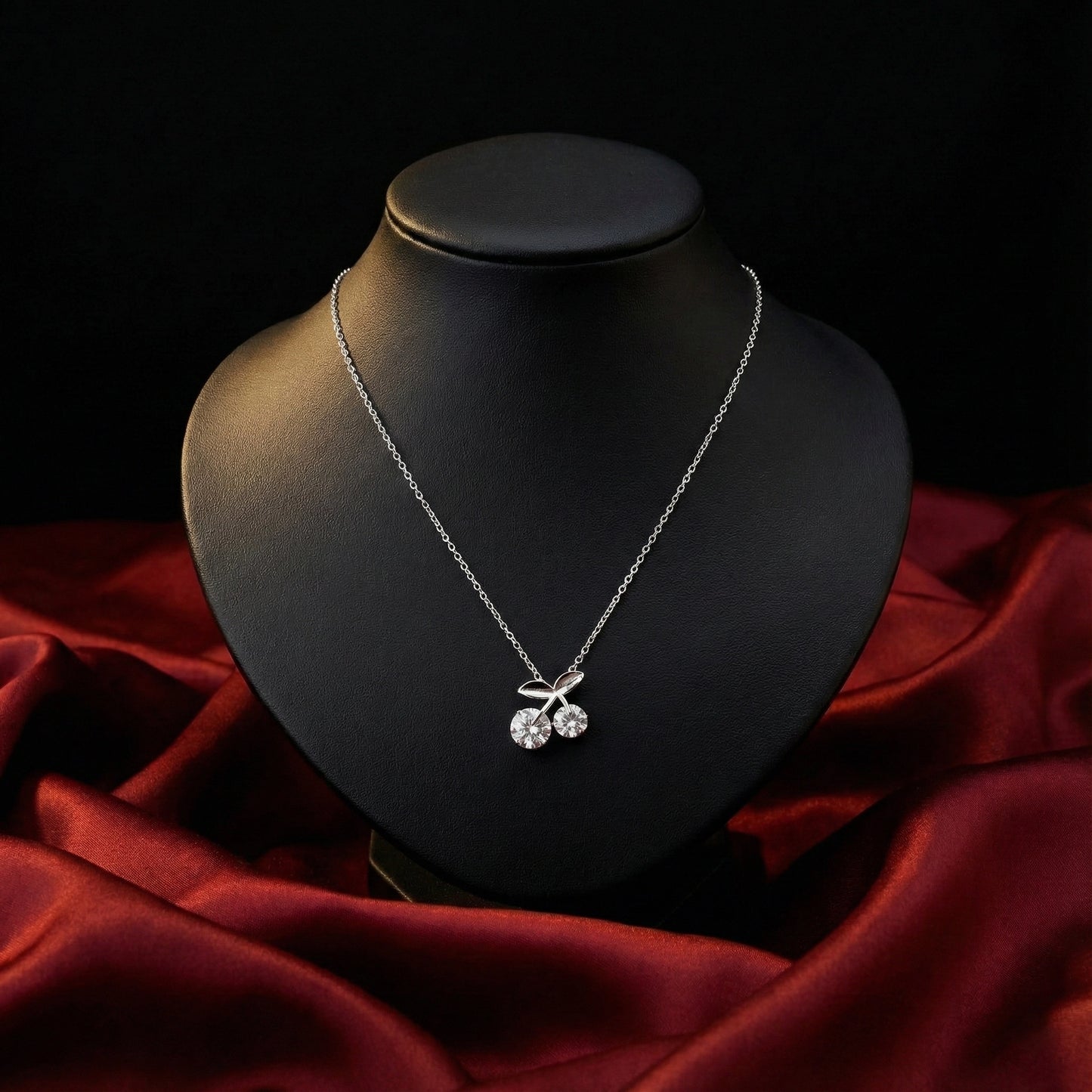 Silver necklace with a cherry pendant on a black mannequin bust against a red fabric background