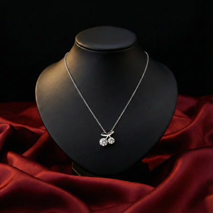 Silver necklace with a cherry pendant on a black mannequin bust against a red fabric background