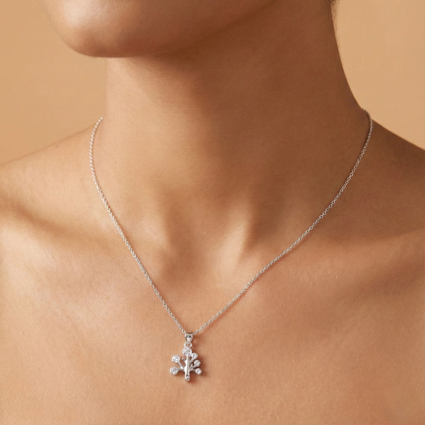 Silver necklace with a pendant on a person's neck against a beige background