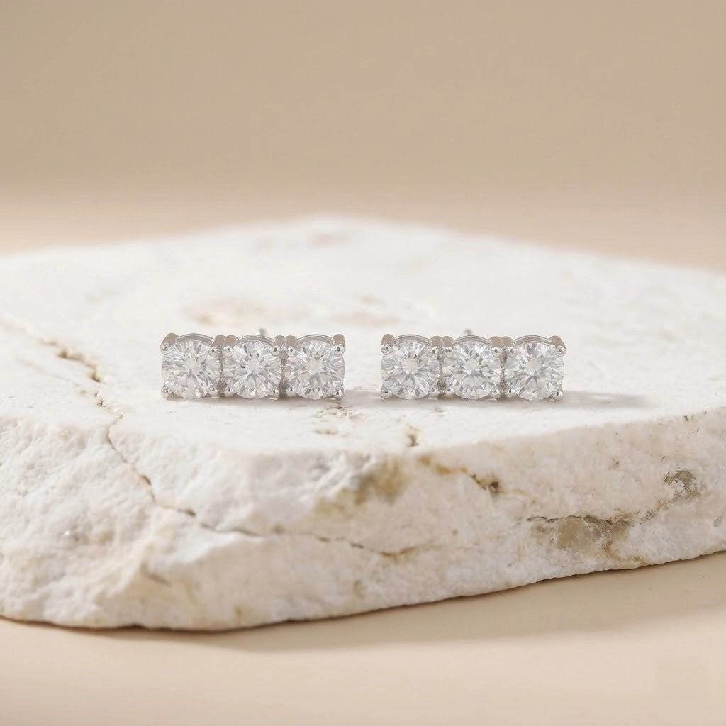 Pair of diamond stud earrings on a textured stone surface with a beige background