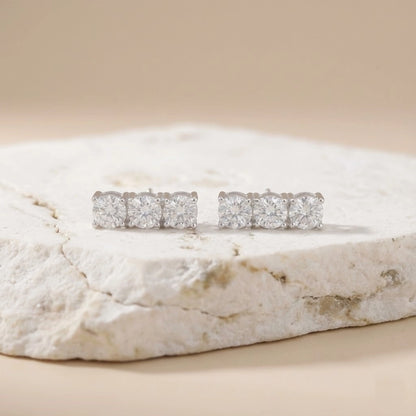 Pair of diamond stud earrings on a textured stone surface with a beige background