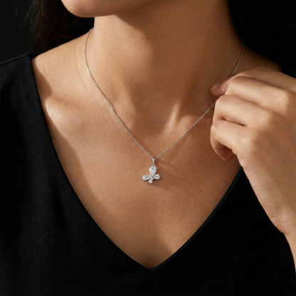 Person wearing a silver necklace with a butterfly pendant against a black background