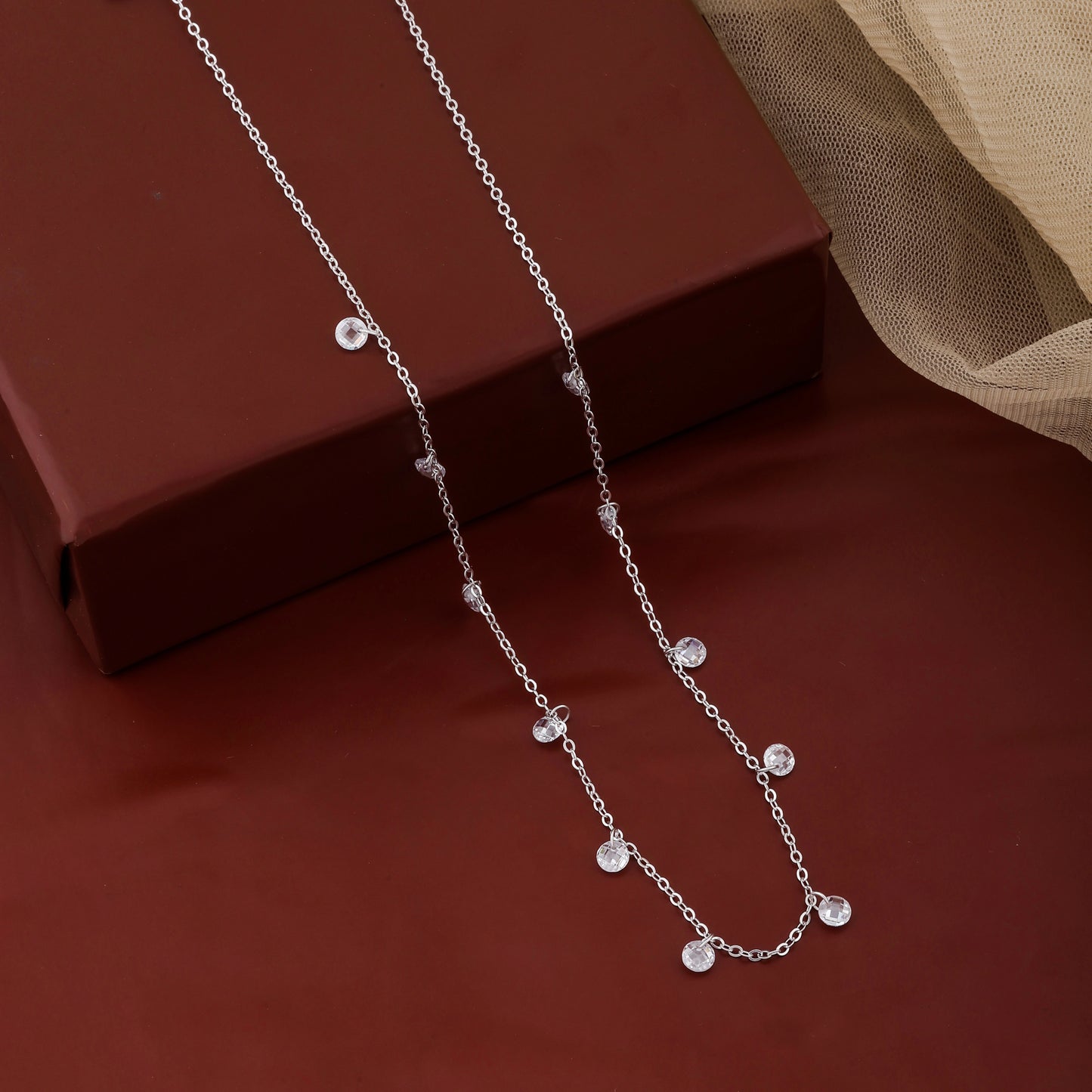 Silver necklace with small beads on a red surface