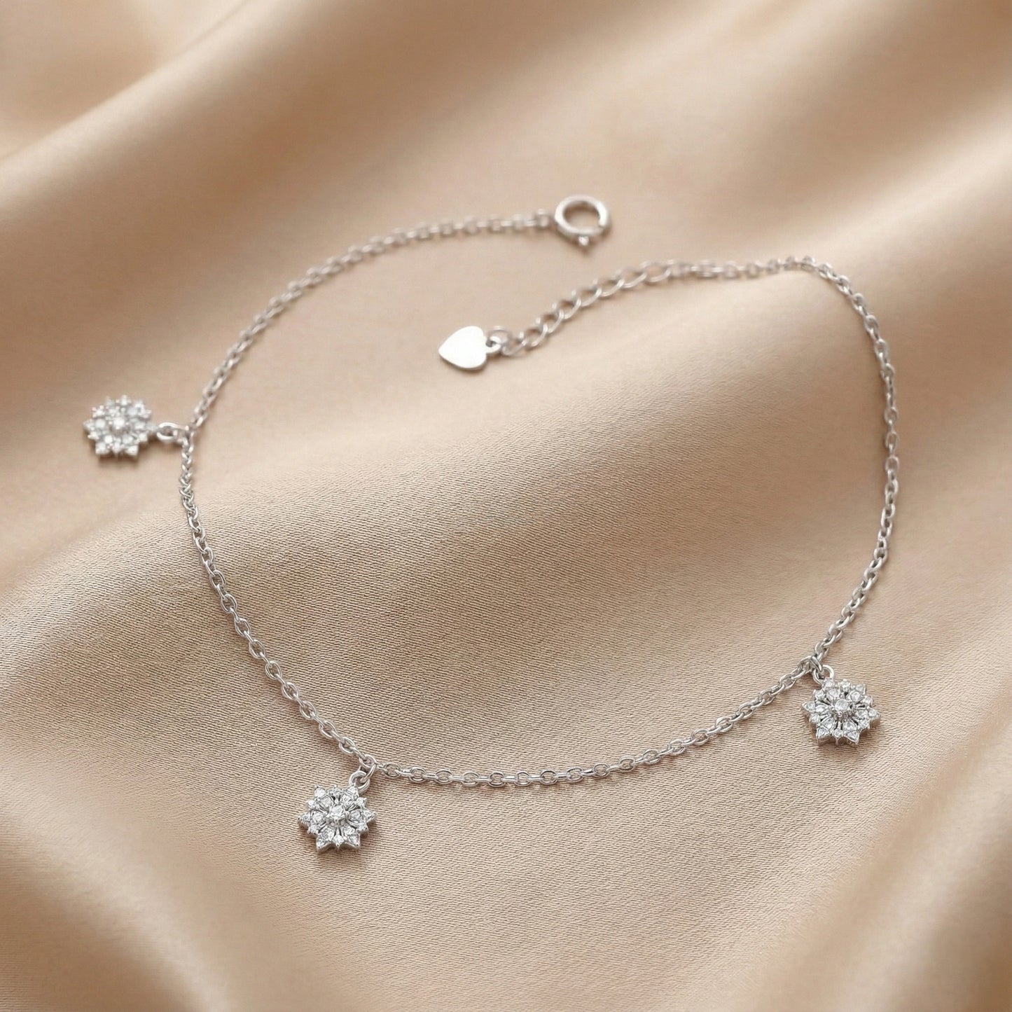 Silver bracelet with floral charms on a beige fabric background