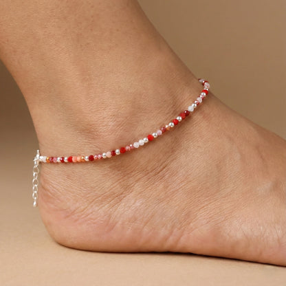 Ankle bracelet with red and white beads on a foot against a beige background
