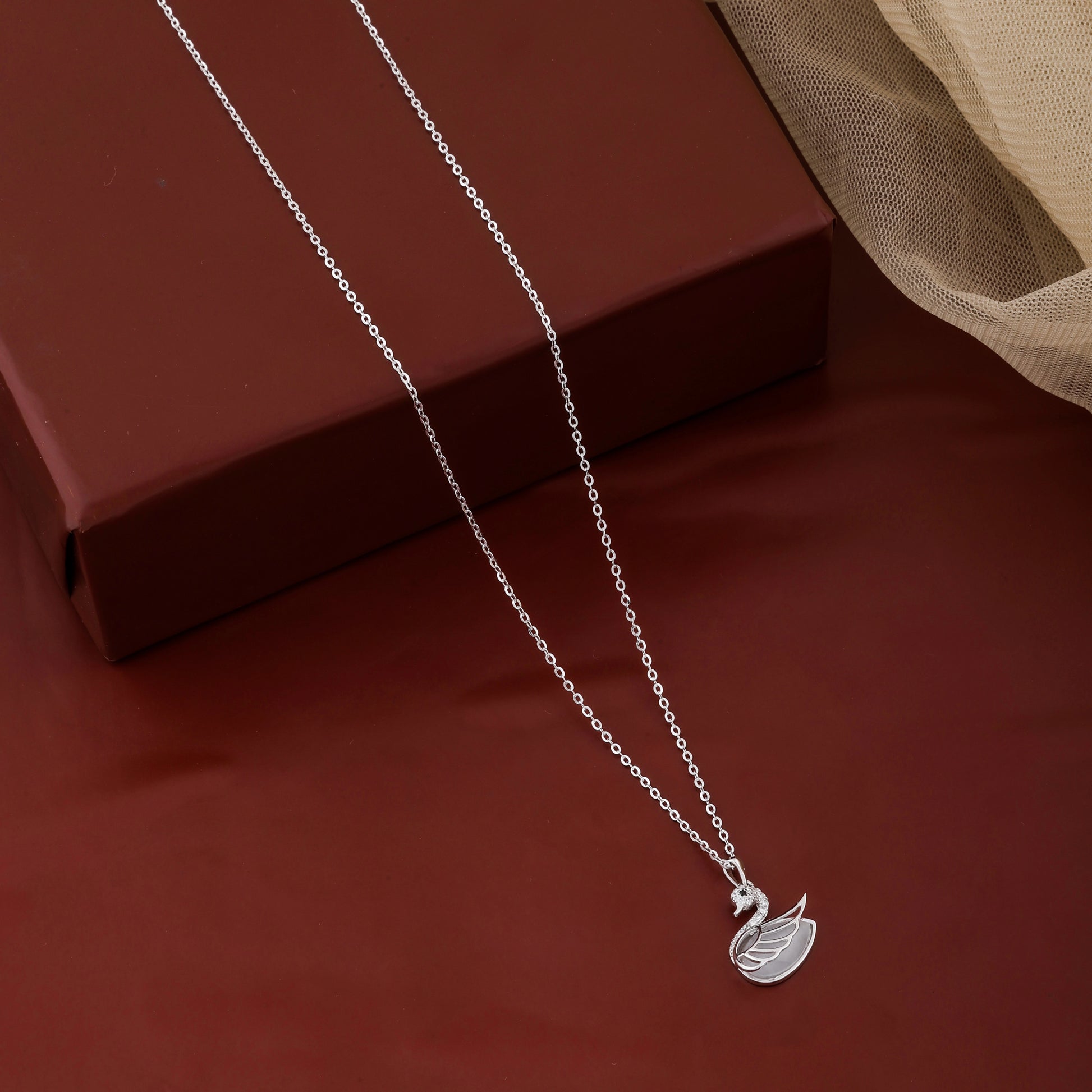 Silver necklace with a leaf pendant on a red surface