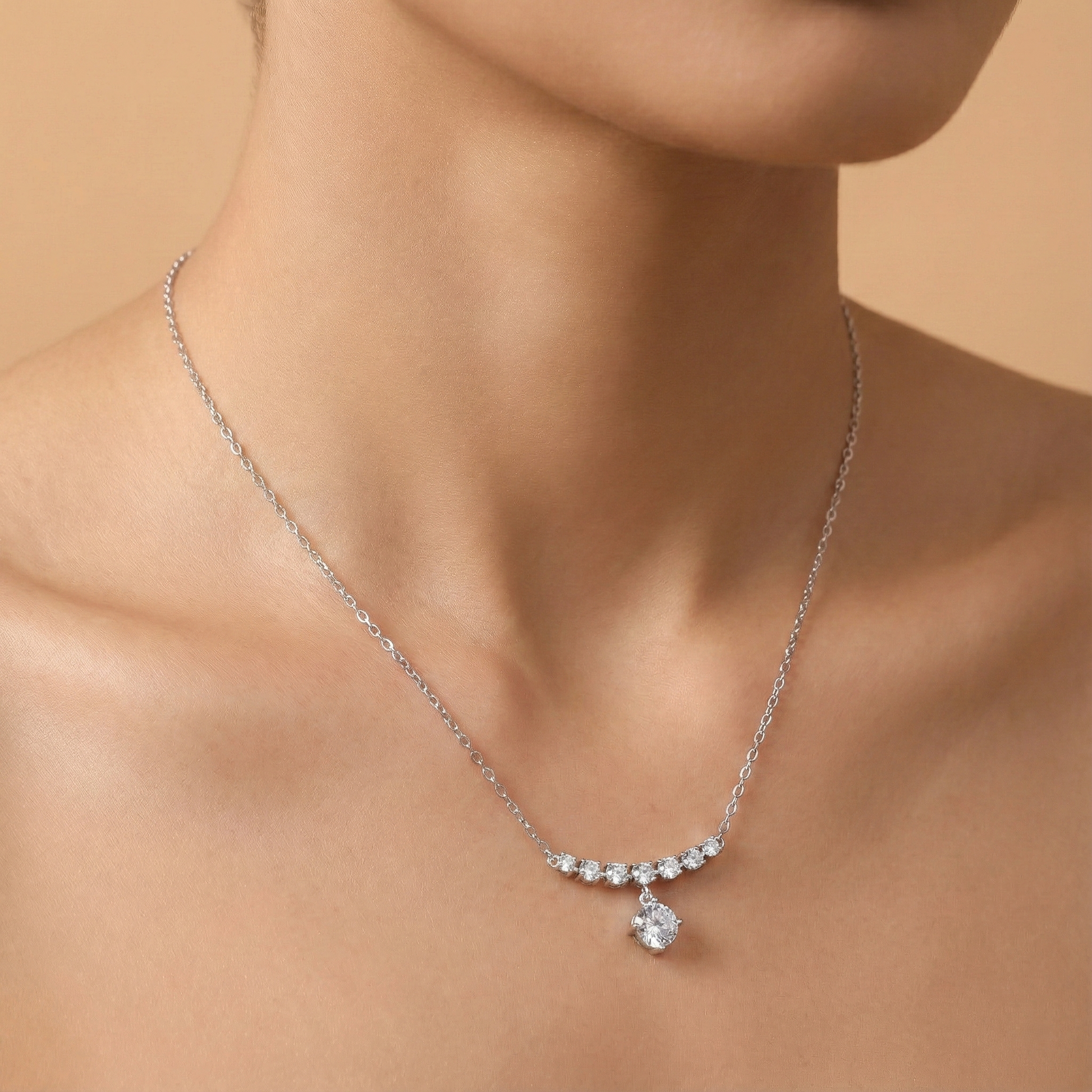 Silver necklace with a pendant on a person's neck against a beige background