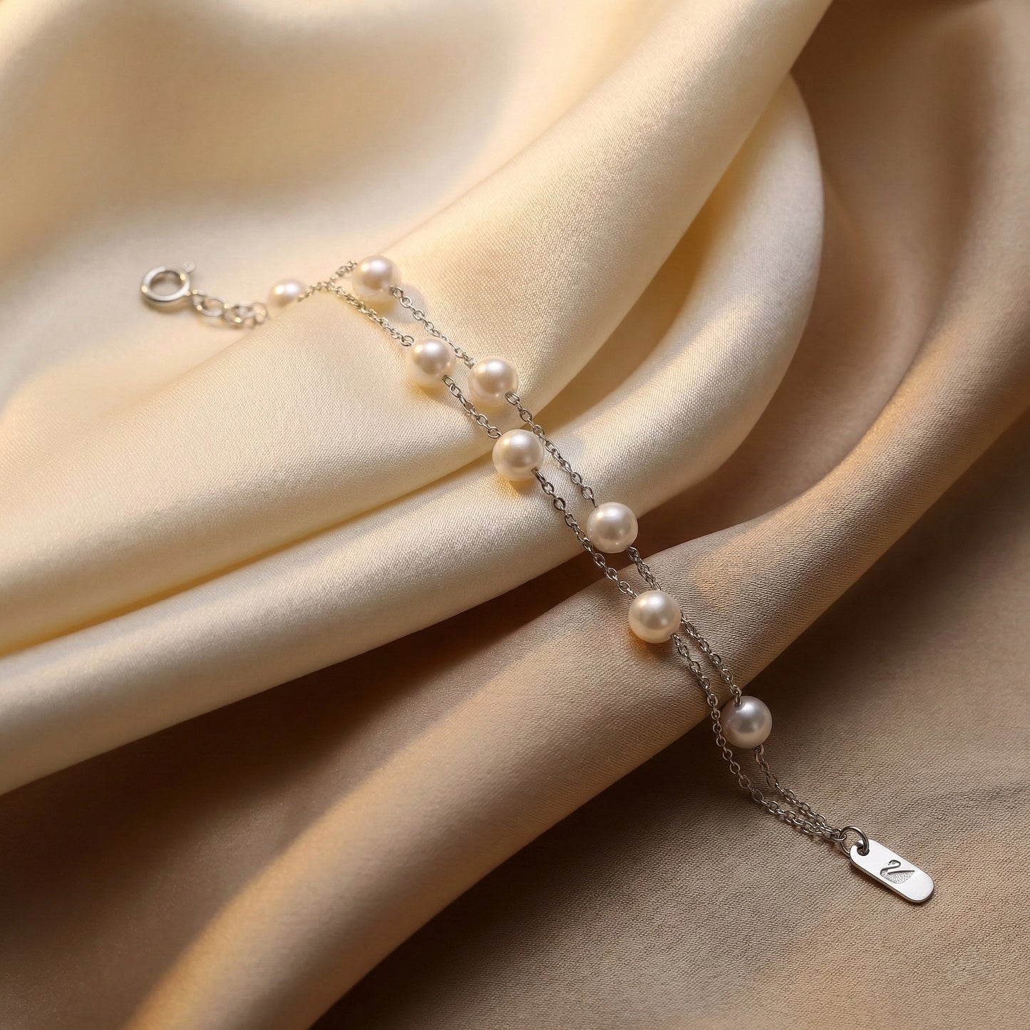 Dainty pearl bracelet with adjustable clasp photographed on beige silk