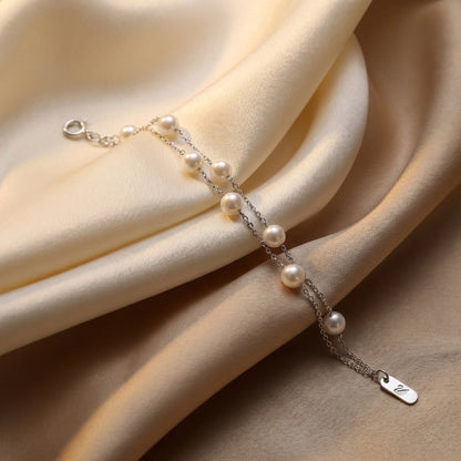 Dainty pearl bracelet with adjustable clasp photographed on beige silk