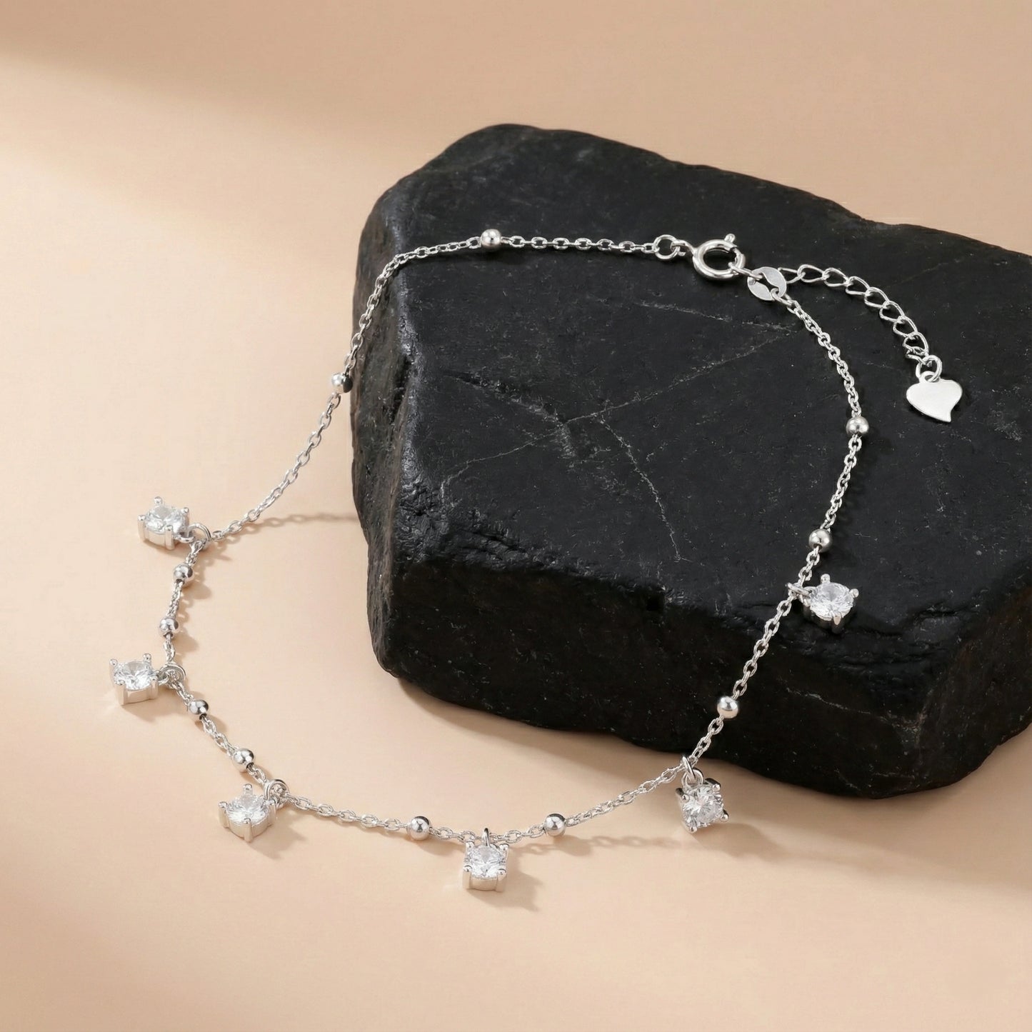 Silver bracelet with heart and clear bead charms on a black stone with a beige background