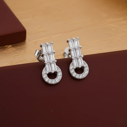 Pair of silver earrings with clear stones on a brown surface