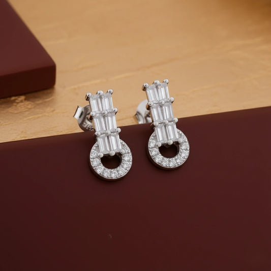 Pair of silver earrings with clear stones on a brown surface
