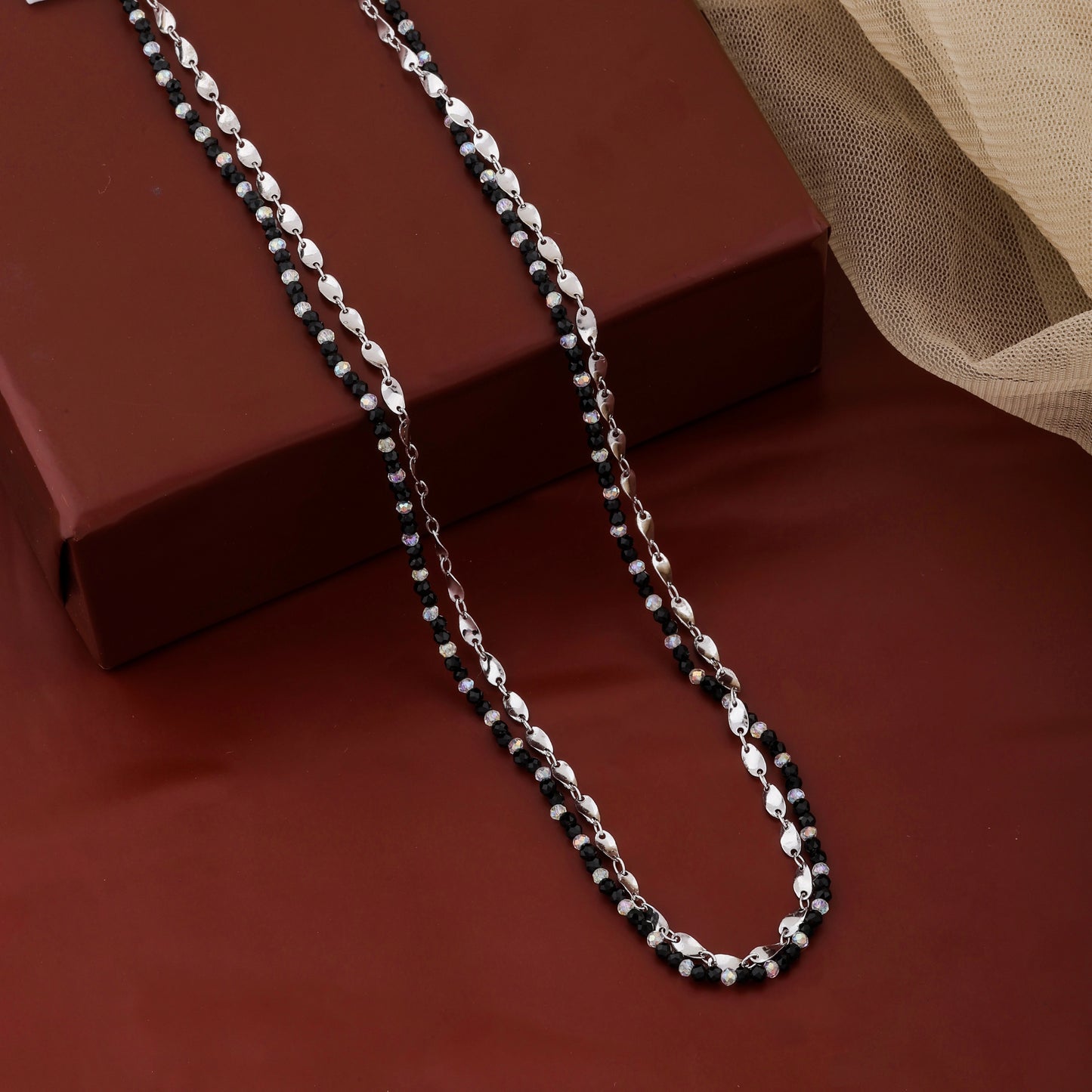 Silver chain necklace on a red surface with a brown box in the background