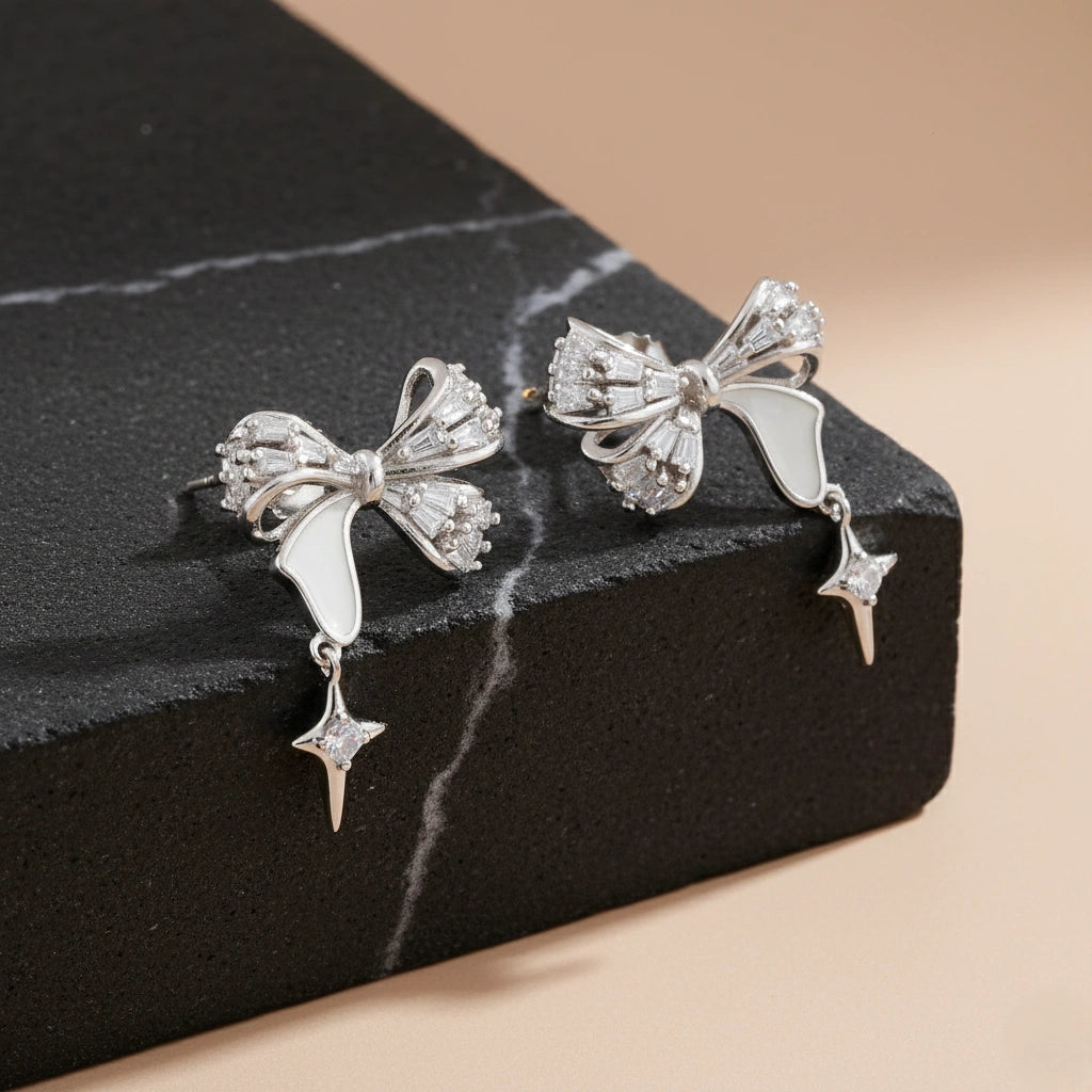 Silver bow-shaped earrings with star details on a black marble surface.