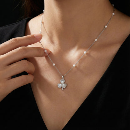 Pearl necklace with a clover-shaped pendant worn by a person against a black background