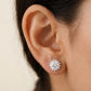 Close-up of an ear wearing a diamond stud earring with a neutral background