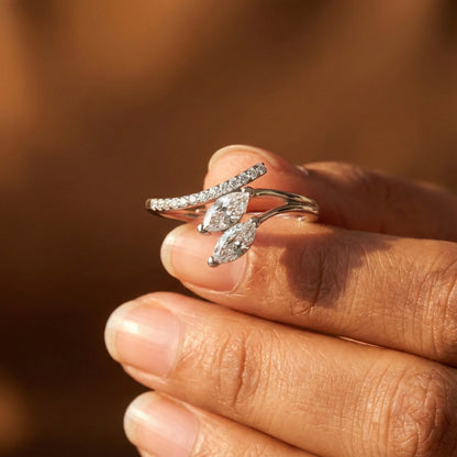 Close-up of a hand wearing a silver ring with marquise-shaped gemstones against a blurred background.