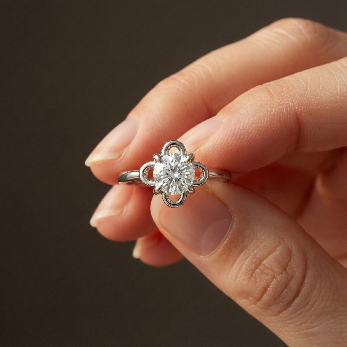 Silver ring with a diamond held in a hand against a dark background