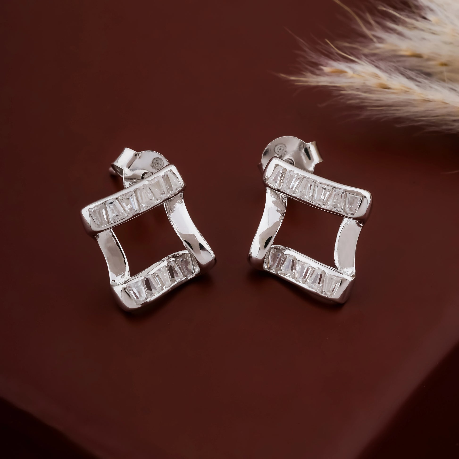 Pair of silver earrings on a brown surface with a feather