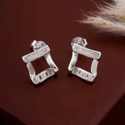 Pair of silver earrings on a brown surface with a feather