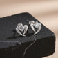 Heart-shaped silver earrings with clear stones on a black stone surface.