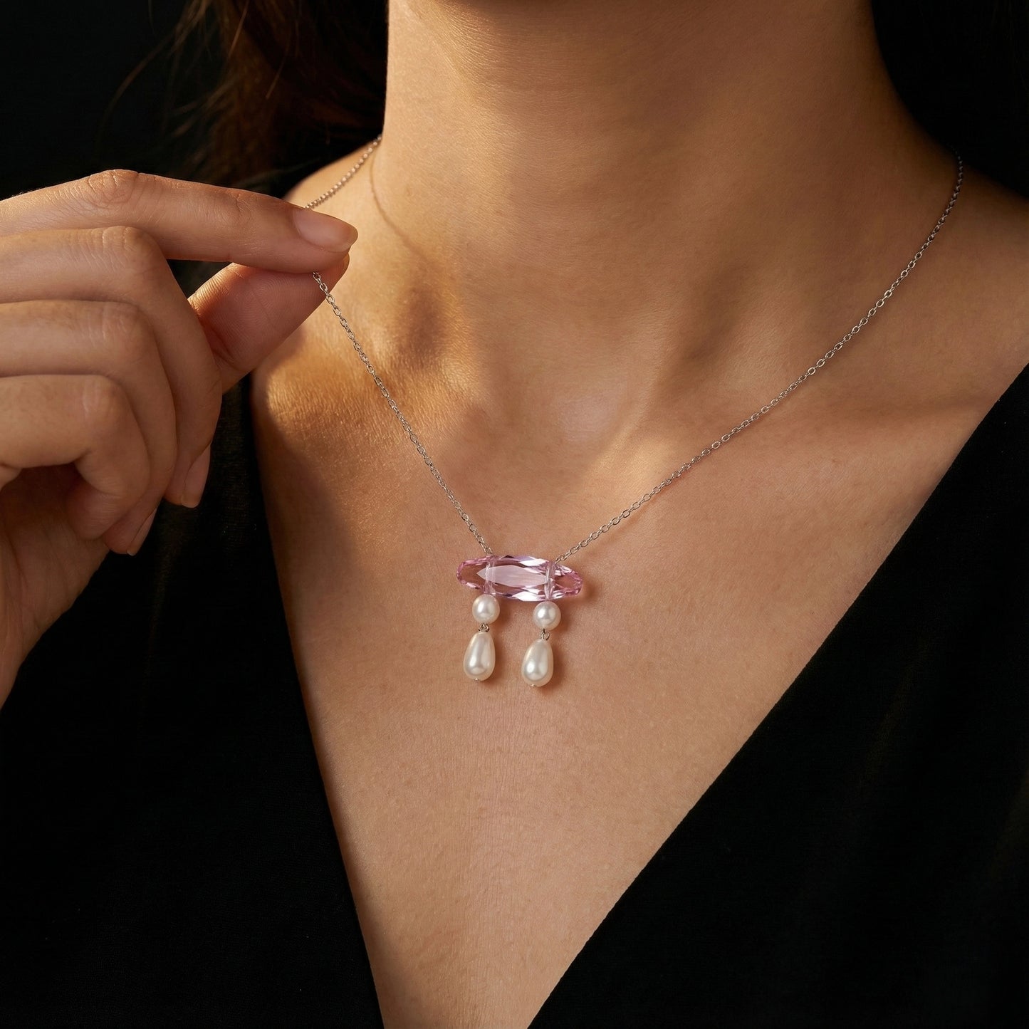 Necklace with a pink gemstone and pearl drops being worn by a person.