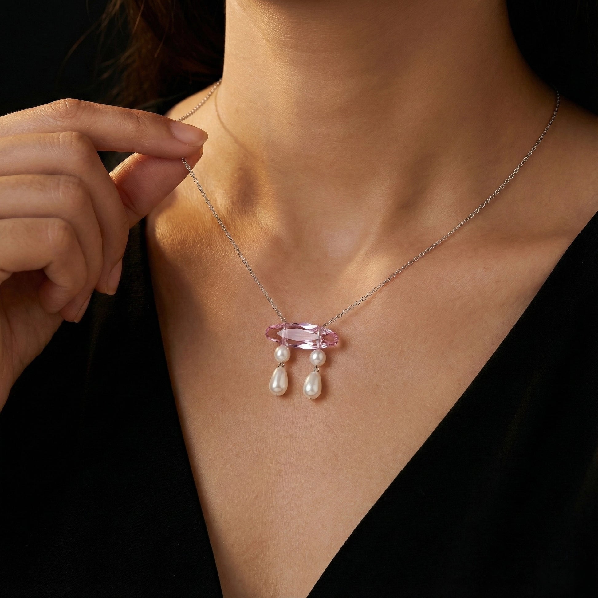 Necklace with a pink gemstone and pearl drops being worn by a person.