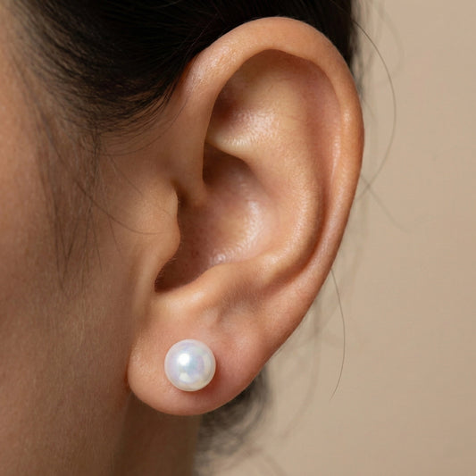 Close-up of white pearl stud earrings with glossy finish on brown background