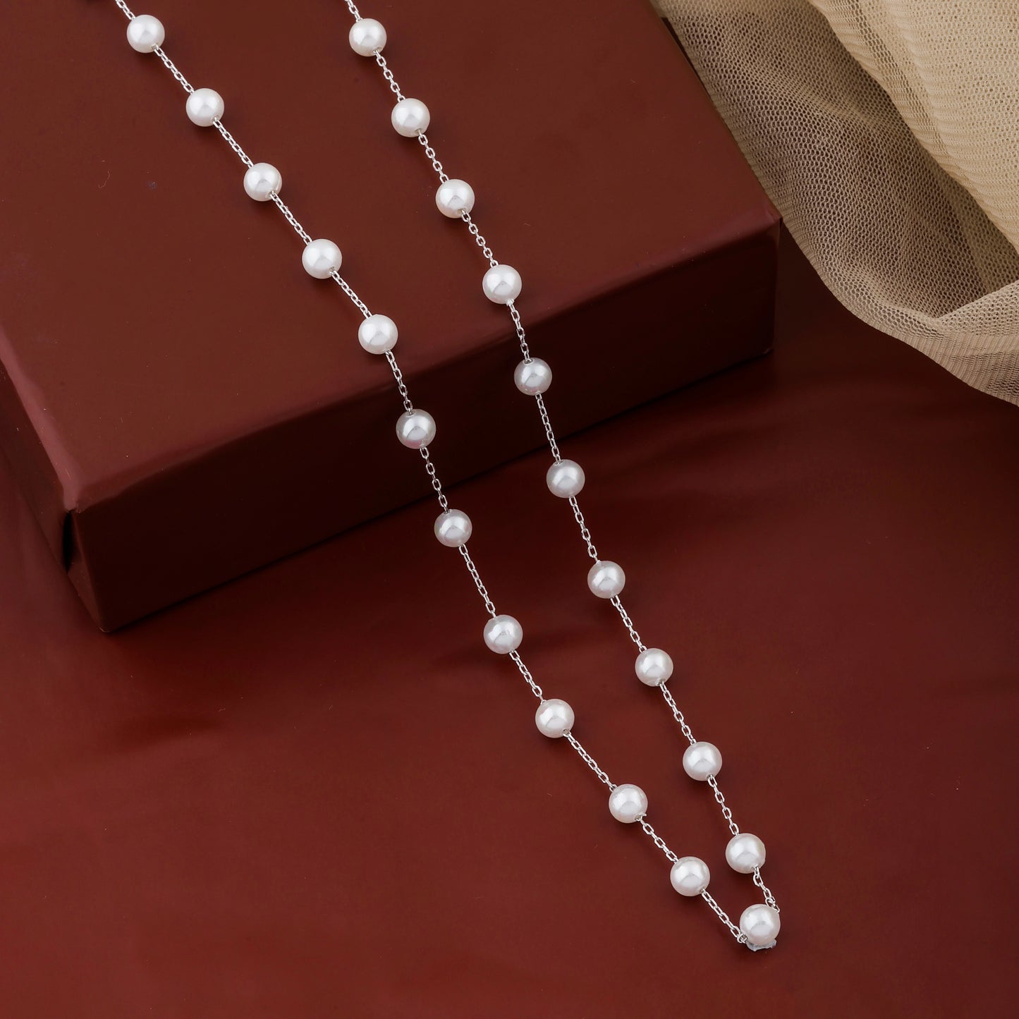 Pearl necklace on a red surface with a brown box in the background