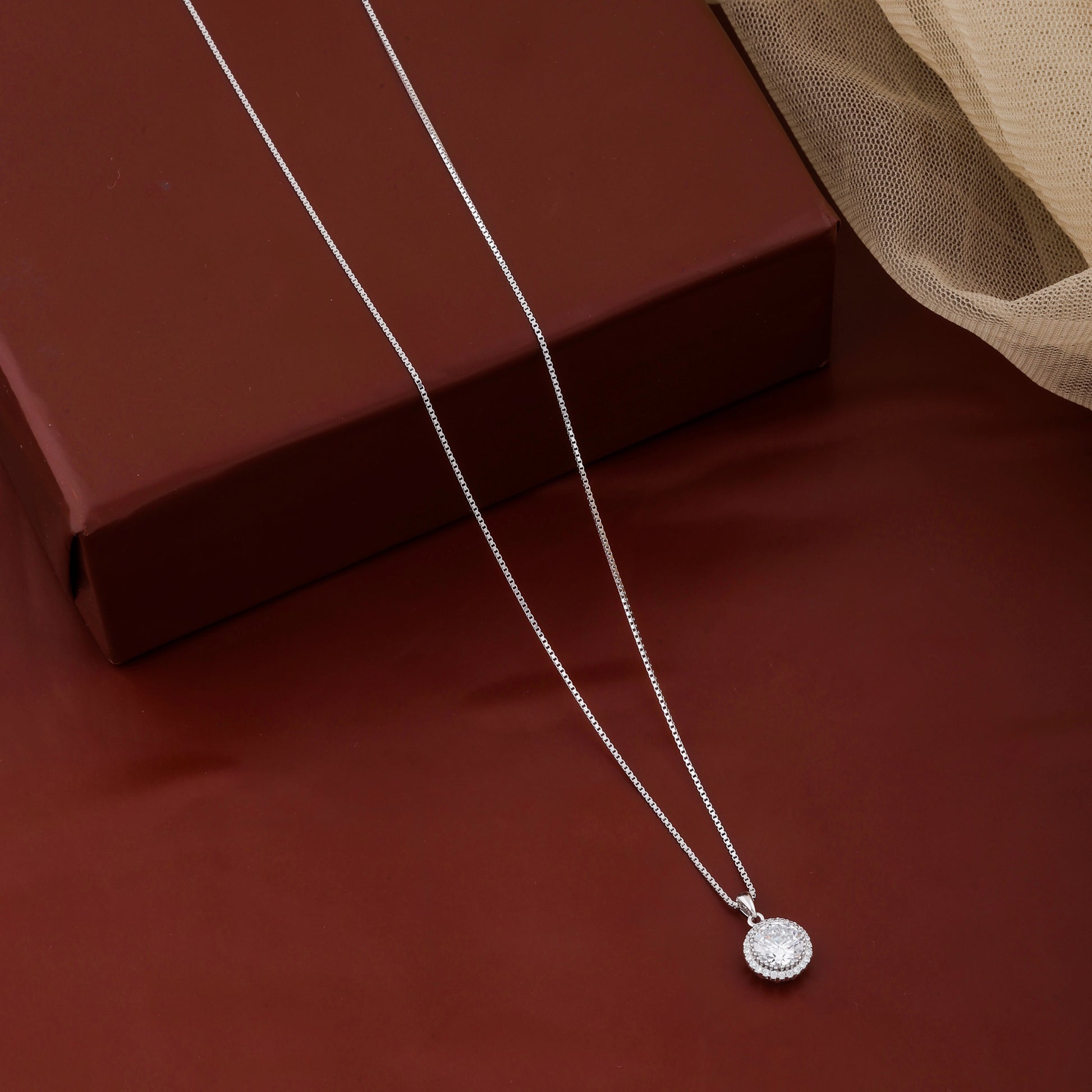 Silver necklace with a round pendant on a red surface