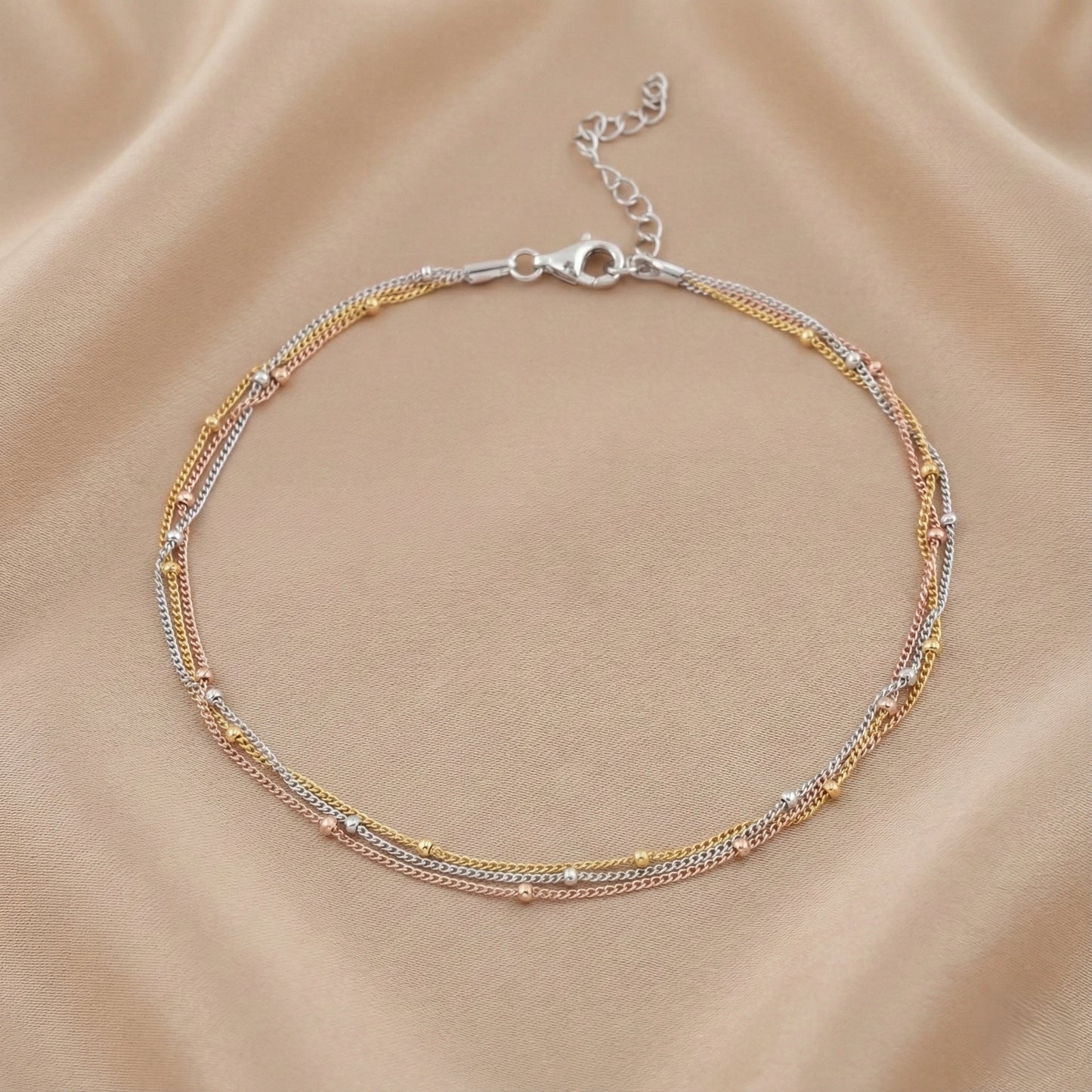 Multistrand bracelet with gold and silver accents on a beige fabric background