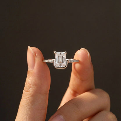 Diamond ring held between two fingers against a dark background