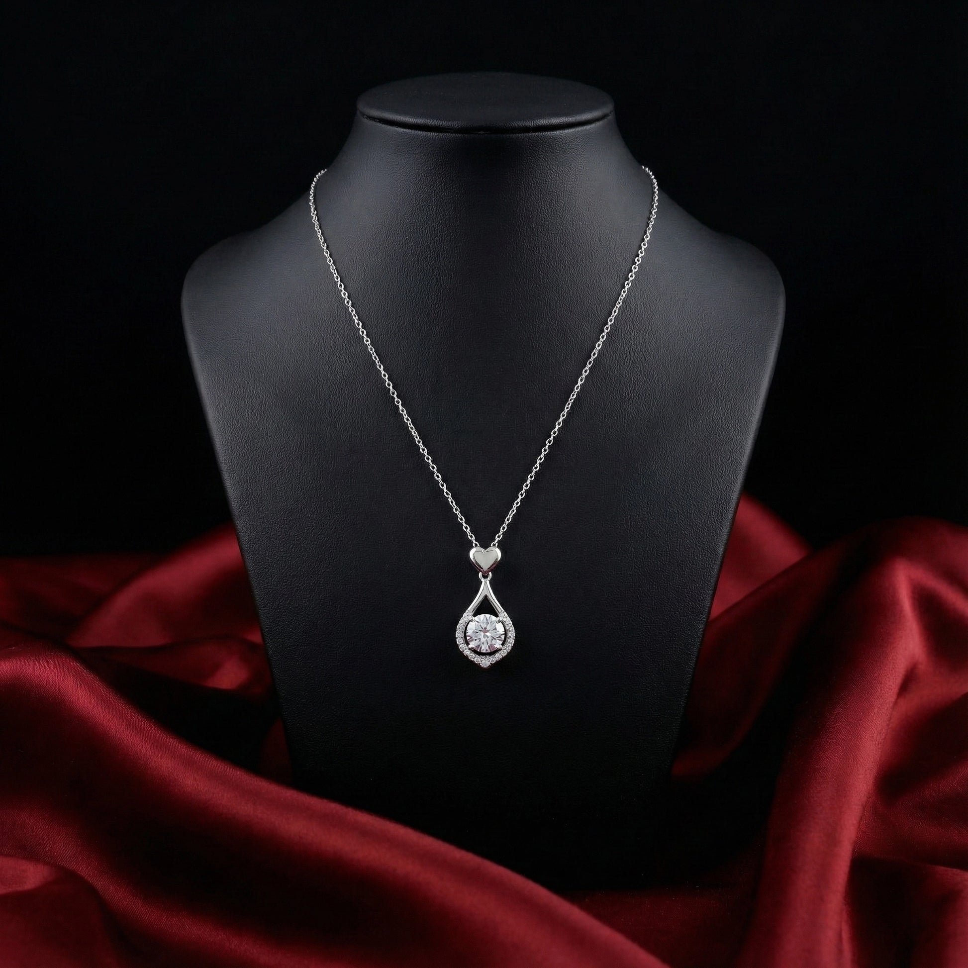 Silver necklace with a heart-shaped pendant on a black mannequin bust against a dark background.