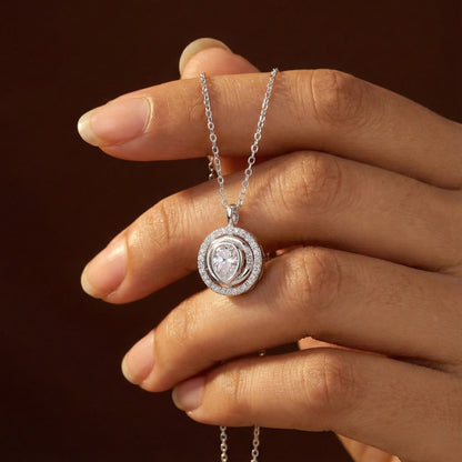 Hand holding a silver necklace with a diamond pendant against a dark background